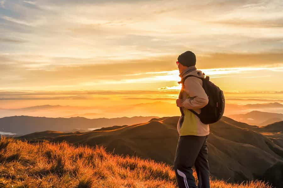 A hiker on a summit ridge at first light, above a sea of cloud